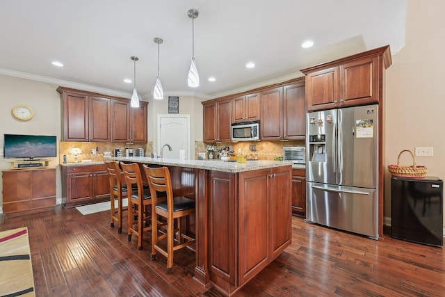 kitchen with hanging light fixtures, appliances with stainless steel finishes, dark hardwood / wood-style flooring, light stone countertops, and a kitchen island with sink