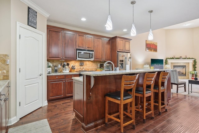 kitchen with stainless steel appliances, tasteful backsplash, a center island with sink, and decorative light fixtures