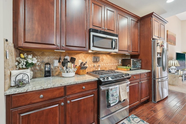 kitchen featuring dark wood-type flooring, appliances with stainless steel finishes, light stone counters, and backsplash