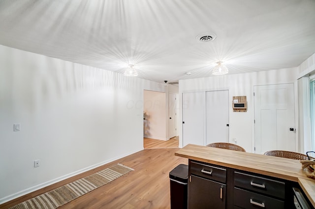 interior space with dark brown cabinets, black dishwasher, wood counters, and light hardwood / wood-style flooring