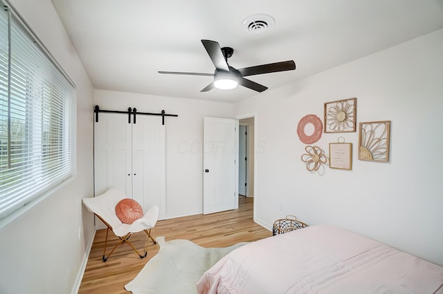 bedroom featuring ceiling fan, a barn door, a closet, and light wood-type flooring