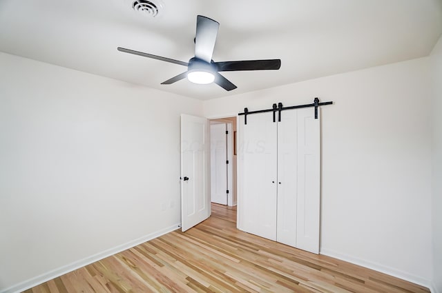 unfurnished bedroom with a closet, light hardwood / wood-style floors, a barn door, and ceiling fan