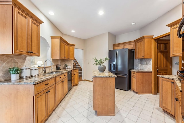 kitchen with sink, light stone counters, black appliances, a kitchen island, and backsplash