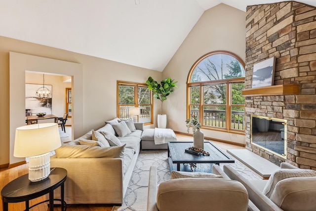 living room featuring an inviting chandelier, hardwood / wood-style floors, a stone fireplace, and high vaulted ceiling