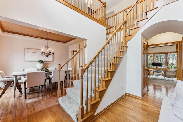 stairs with hardwood / wood-style flooring, an inviting chandelier, a towering ceiling, a tray ceiling, and ornamental molding