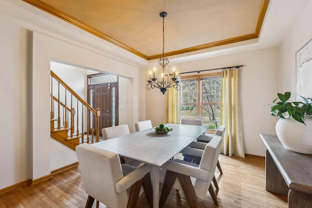 dining area featuring an inviting chandelier, ornamental molding, a tray ceiling, and light hardwood / wood-style flooring