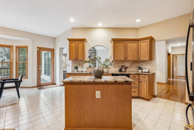 kitchen with decorative backsplash, a center island, light stone countertops, and light tile patterned floors