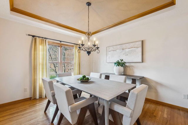 dining area with crown molding, a tray ceiling, and light hardwood / wood-style floors