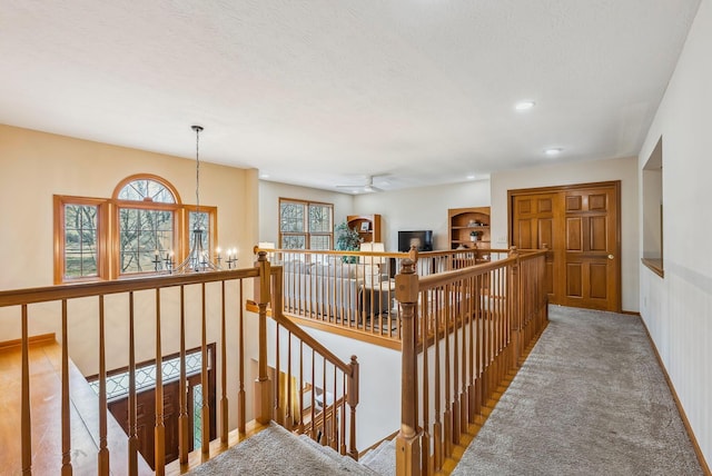 hall with a healthy amount of sunlight, light colored carpet, a textured ceiling, and an inviting chandelier