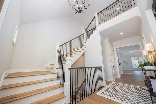 stairs featuring crown molding, a towering ceiling, hardwood / wood-style floors, and a notable chandelier