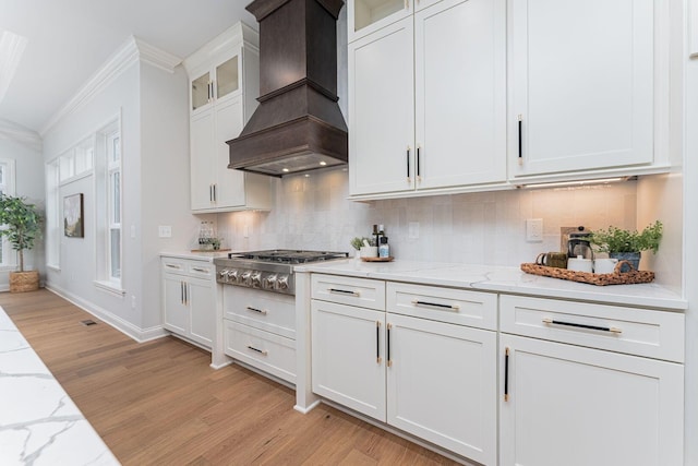 kitchen with stainless steel gas cooktop, custom exhaust hood, white cabinetry, ornamental molding, and light stone countertops