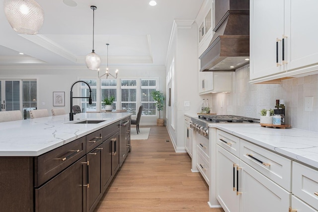 kitchen with premium range hood, sink, white cabinetry, crown molding, and a tray ceiling