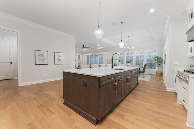 kitchen featuring a center island with sink, sink, hanging light fixtures, and white cabinets