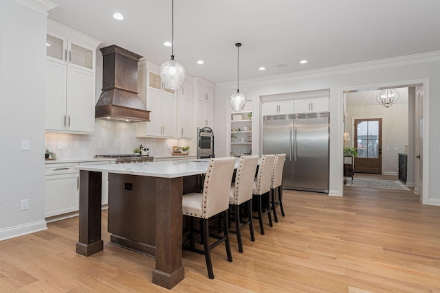 kitchen featuring pendant lighting, stainless steel appliances, white cabinets, a center island with sink, and custom exhaust hood