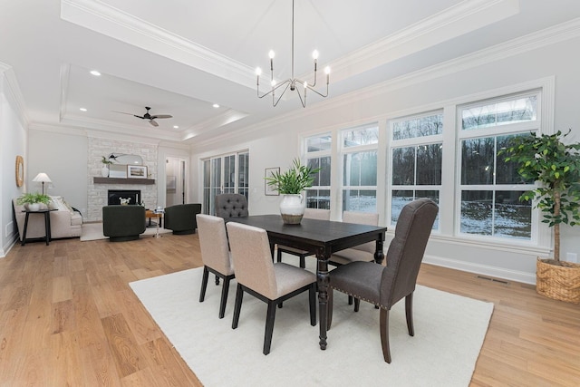 dining space with a fireplace, plenty of natural light, a tray ceiling, and light hardwood / wood-style floors