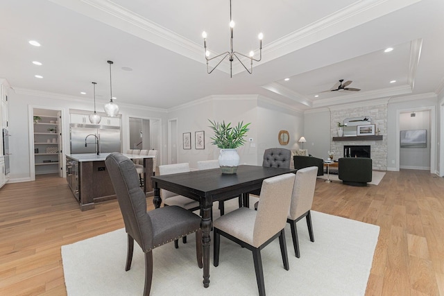 dining room with light hardwood / wood-style flooring, ceiling fan, a tray ceiling, a fireplace, and ornamental molding