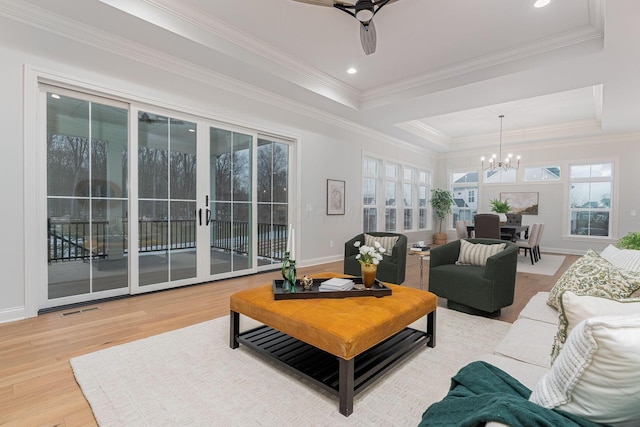 living room with crown molding, wood-type flooring, a tray ceiling, and ceiling fan with notable chandelier