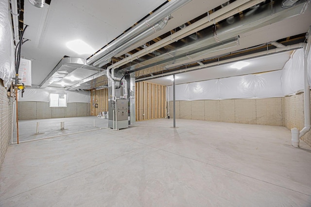 basement featuring brick wall and heating unit