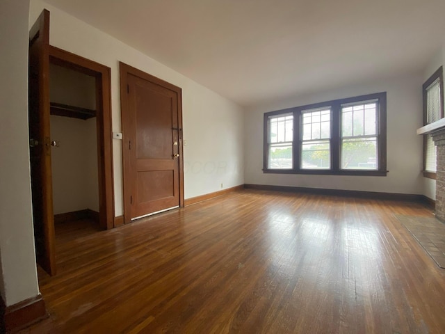 unfurnished room with a brick fireplace and dark hardwood / wood-style floors