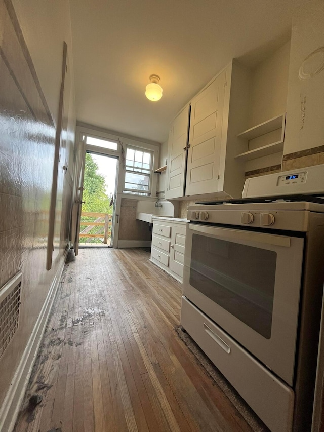 kitchen with white cabinetry, white gas range, sink, and hardwood / wood-style floors