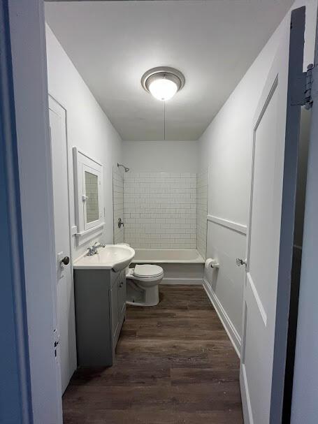 full bathroom with hardwood / wood-style flooring, tiled shower / bath, vanity, and toilet