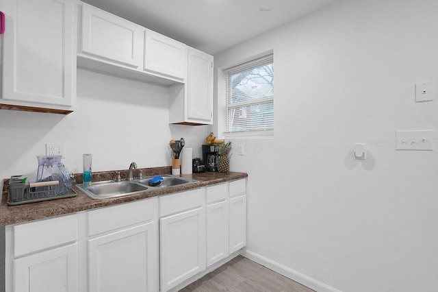 kitchen featuring baseboards, light wood-type flooring, white cabinetry, dark countertops, and a sink