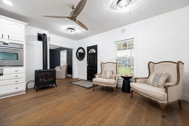 living area featuring hardwood / wood-style flooring, a wood stove, a textured ceiling, and ceiling fan