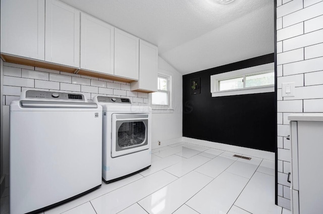 laundry area featuring separate washer and dryer, light tile patterned floors, cabinets, and a textured ceiling