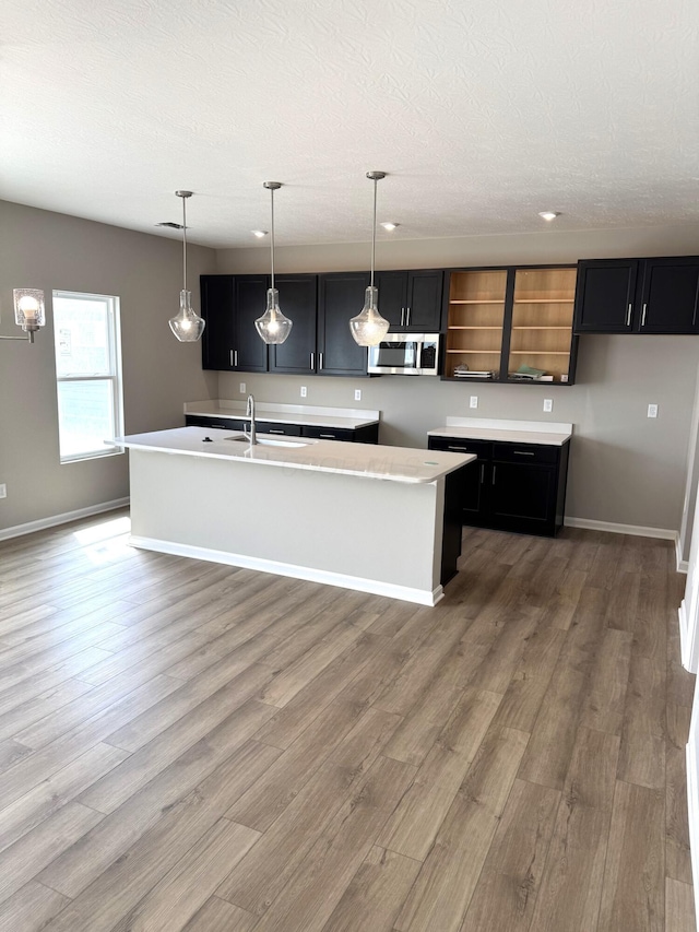 kitchen featuring stainless steel microwave, baseboards, wood finished floors, and a center island with sink