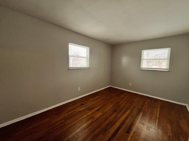 unfurnished room featuring dark wood-style floors, visible vents, and baseboards