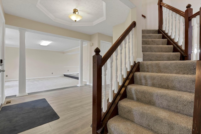 staircase with a tray ceiling, crown molding, decorative columns, wood finished floors, and baseboards