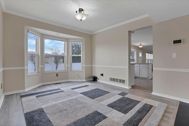 spare room with baseboards, crown molding, visible vents, and wood finished floors