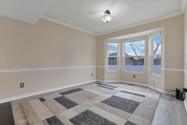 empty room with crown molding, wood finished floors, and baseboards