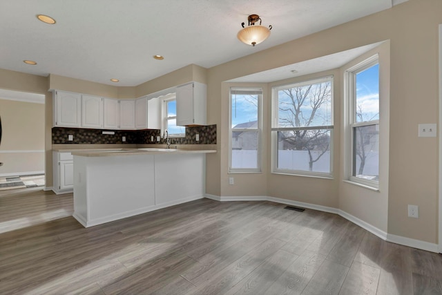 kitchen with visible vents, decorative backsplash, white cabinetry, wood finished floors, and baseboards