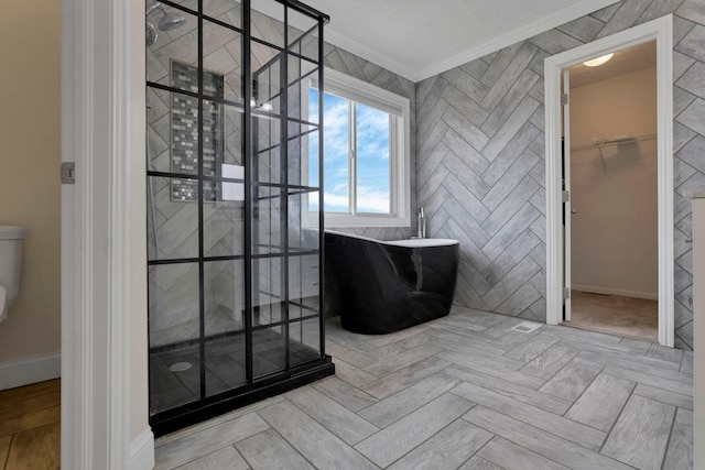 bathroom with baseboards, a soaking tub, a spacious closet, a tile shower, and crown molding