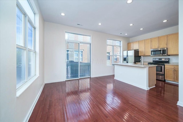 kitchen with dark wood-type flooring, light brown cabinetry, sink, a center island with sink, and appliances with stainless steel finishes