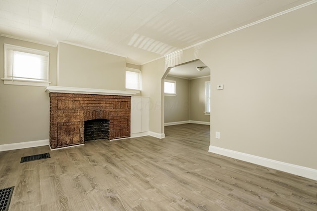 unfurnished living room featuring hardwood / wood-style flooring, ornamental molding, and a brick fireplace