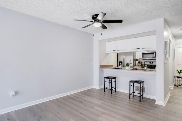 kitchen with a breakfast bar area, light hardwood / wood-style flooring, white cabinetry, stainless steel appliances, and kitchen peninsula