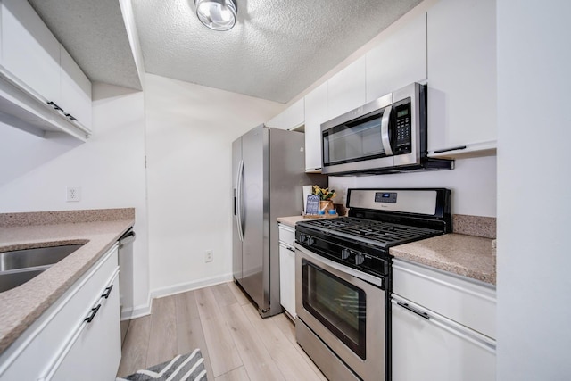 kitchen with sink, a textured ceiling, light wood-type flooring, appliances with stainless steel finishes, and white cabinets