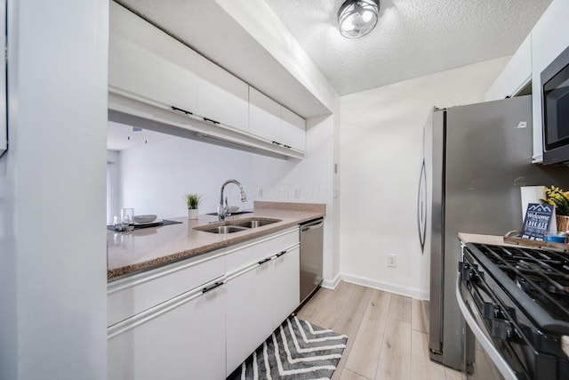 kitchen featuring sink, white cabinetry, stainless steel appliances, a textured ceiling, and light wood-type flooring