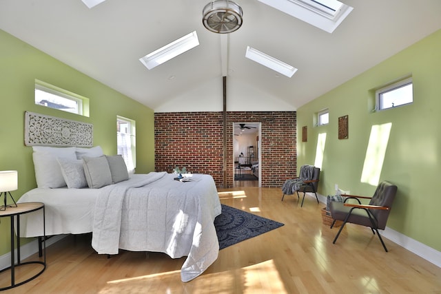 bedroom featuring a skylight, high vaulted ceiling, brick wall, and light wood-type flooring