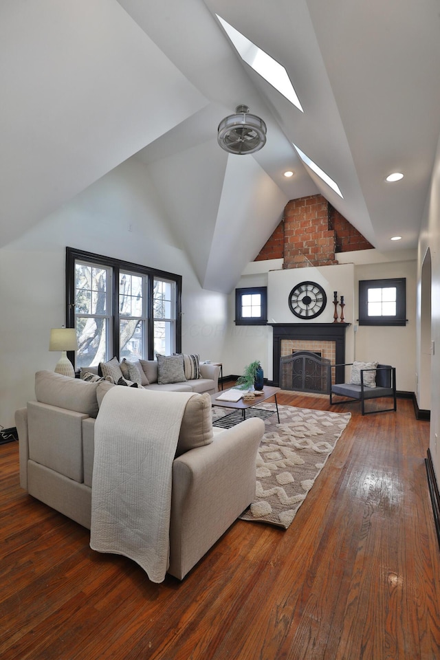 living room with a large fireplace, a healthy amount of sunlight, dark hardwood / wood-style flooring, and vaulted ceiling with skylight