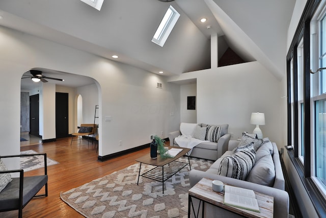 living room with hardwood / wood-style flooring, a healthy amount of sunlight, high vaulted ceiling, and a skylight