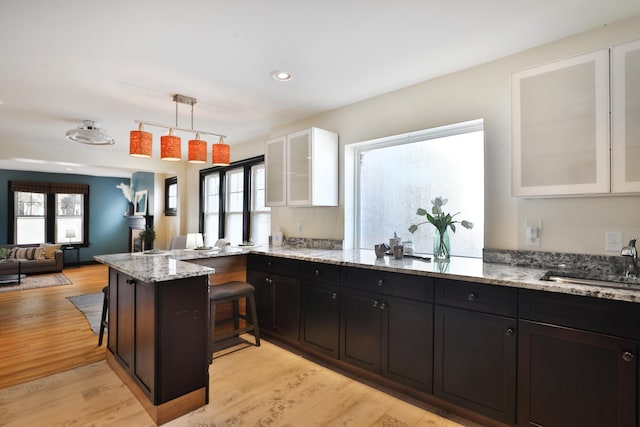 kitchen with sink, white cabinetry, light stone counters, a healthy amount of sunlight, and kitchen peninsula