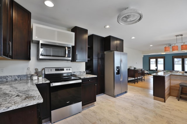 kitchen featuring appliances with stainless steel finishes, pendant lighting, light stone counters, light hardwood / wood-style floors, and dark brown cabinets