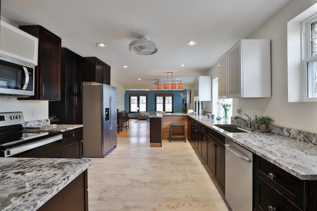 kitchen featuring sink, dark brown cabinets, stainless steel appliances, light stone counters, and light wood-type flooring