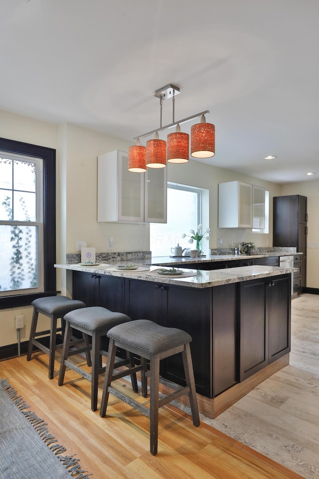 kitchen featuring light hardwood / wood-style flooring, hanging light fixtures, light stone counters, white cabinets, and kitchen peninsula