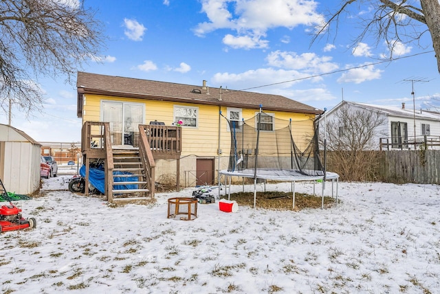 snow covered rear of property featuring a trampoline and a deck