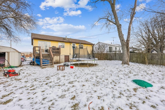 snow covered rear of property with a deck and a trampoline