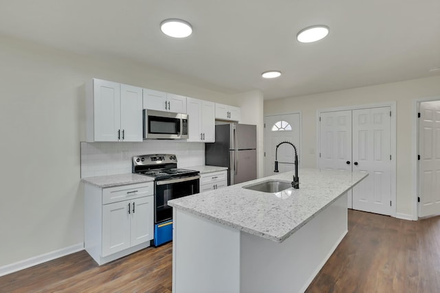 kitchen featuring sink, white cabinetry, stainless steel appliances, light stone counters, and a center island with sink